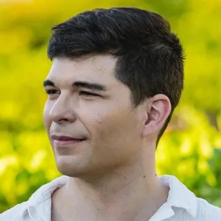 Profile view of Pier-Luc Charbonneau, with short dark hair and a white shirt, against a blurred green background.